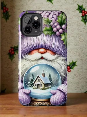 A phone case featuring a winter scene with a snow globe containing a house and trees, along with a purple knitted hat and holly leaves.