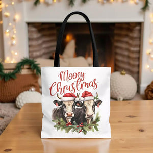 A white tote bag with a Christmas-themed design featuring two cows wearing Santa hats, surrounded by holly and berries.