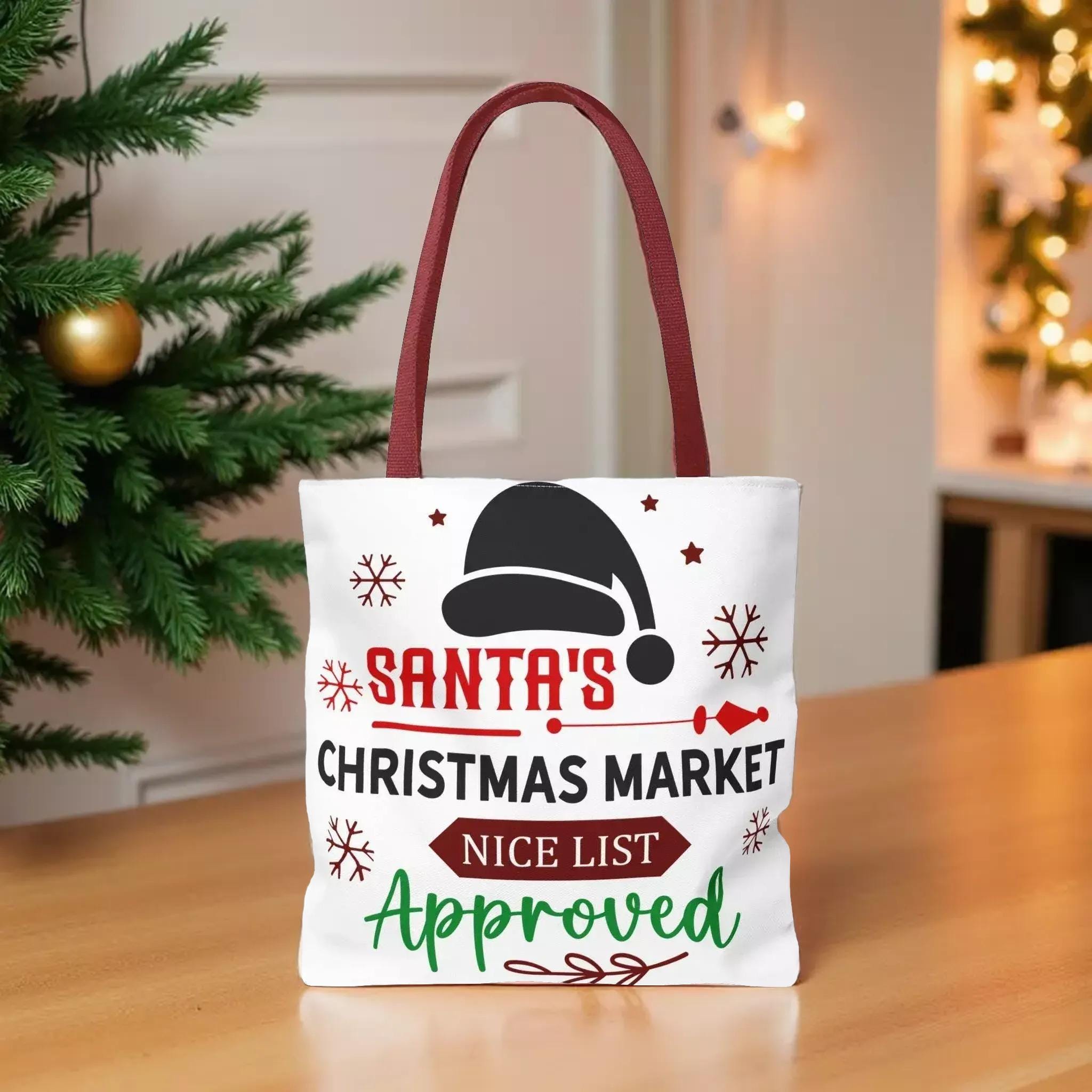 A white tote bag with a red handle, featuring a Santa hat and snowflakes, placed on a wooden surface.