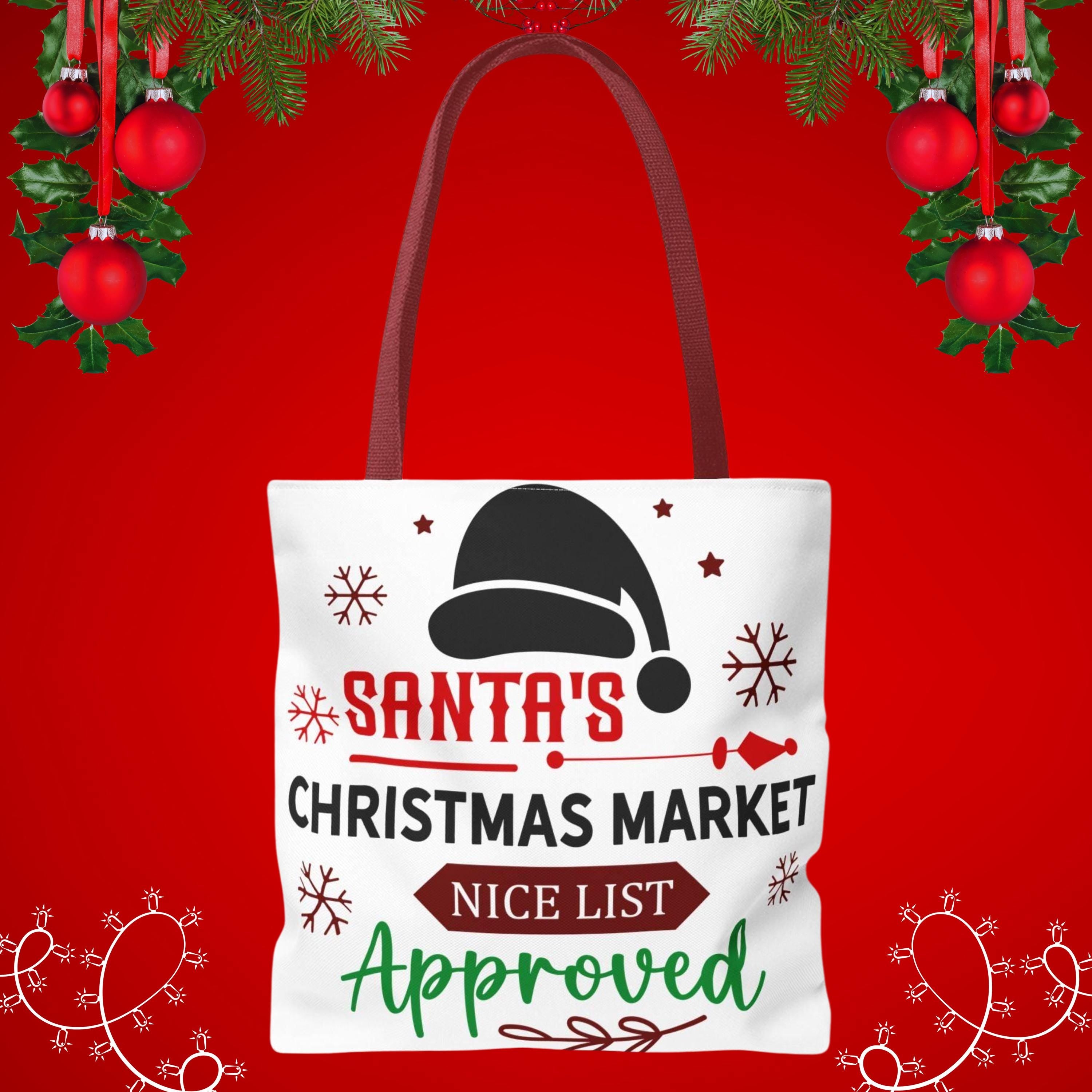 A white tote bag with a Santa hat and snowflakes printed on it, along with the text "Santa's Christmas Market NICE List Approved" against a red background with Christmas ornaments.