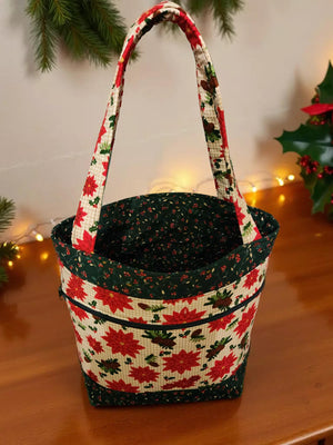 A handbag with a floral pattern and red poinsettia flowers is displayed on a wooden surface, with a Christmas wreath visible in the background.