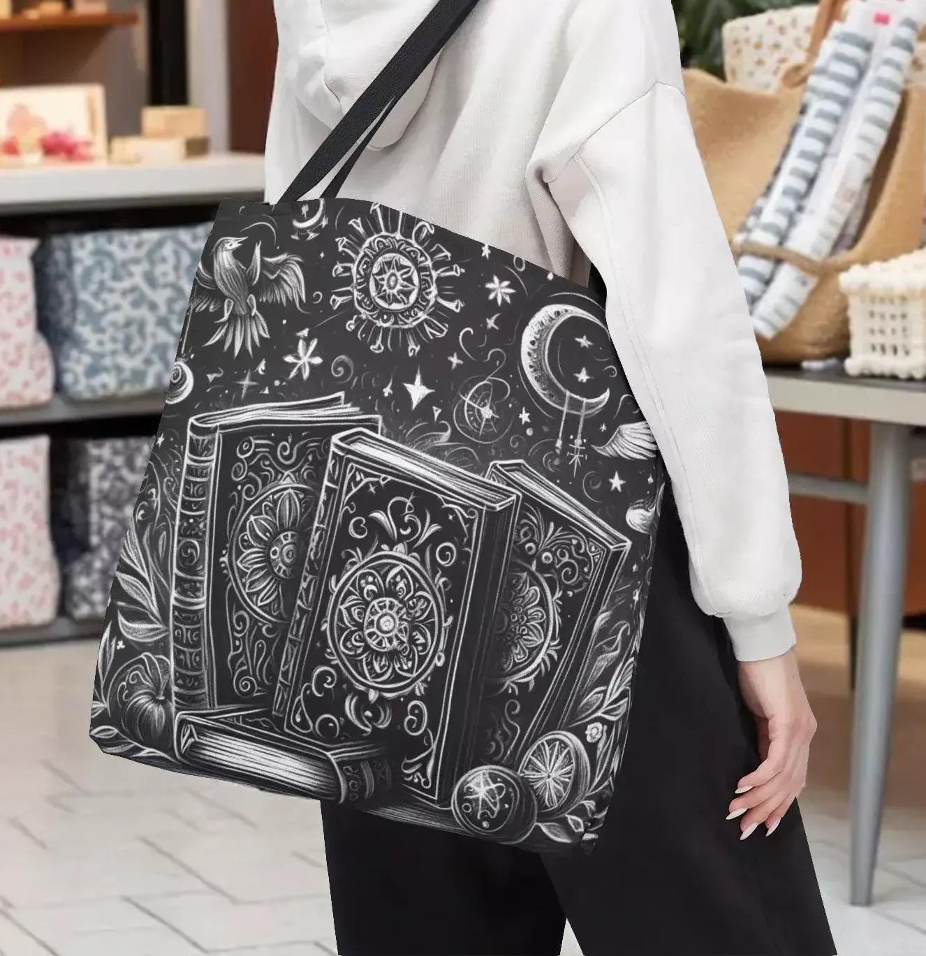 A woman wearing a white cap and carrying a large tote bag with a black and white graphic design featuring books and celestial elements.