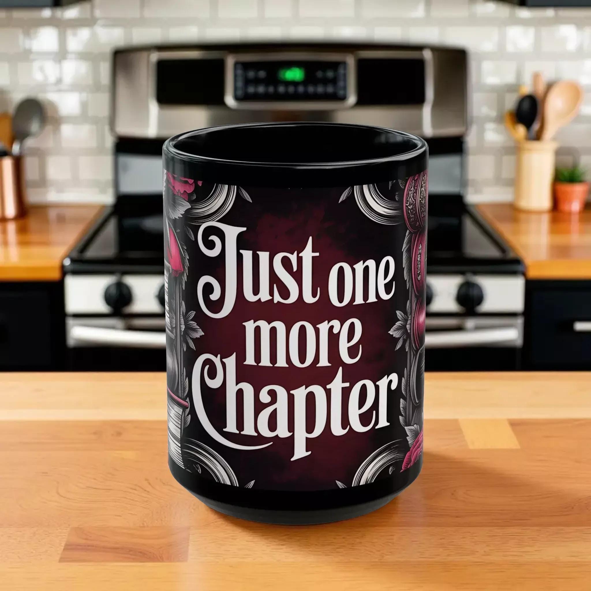 A black coffee mug with a printed design featuring the text "Just one more chapter" in a decorative font.
