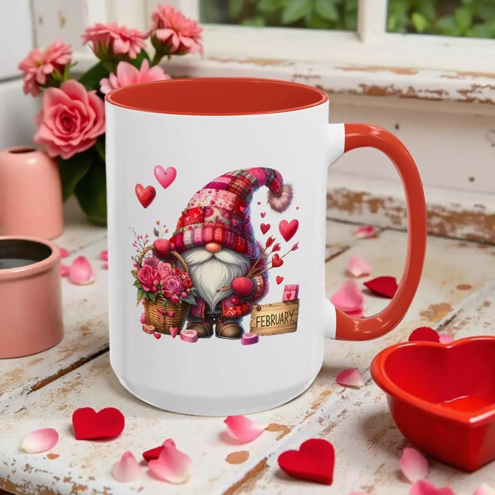 A mug with a graphic of a gnome wearing a red hat and holding flowers, surrounded by hearts and the word "FEBRUARY" on a wooden surface.