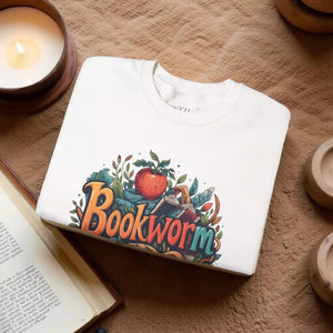 The image is a white t-shirt with a colorful graphic design featuring the word "Book Worm" surrounded by various objects such as an apple, leaves, and a book.