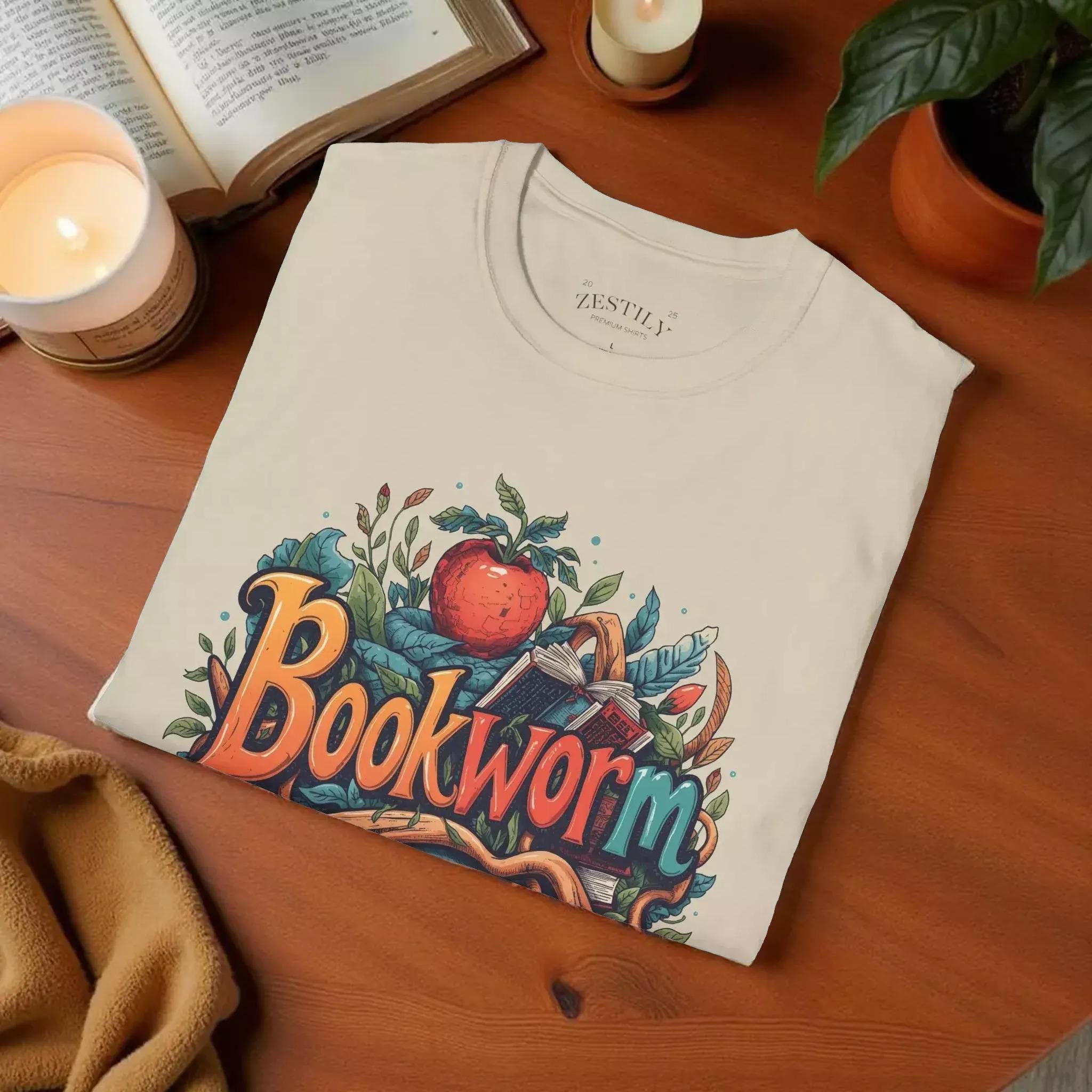 The image is a t-shirt with a colorful graphic design featuring the word "Bookworm" surrounded by various elements such as leaves, an apple, and a book.