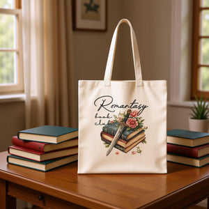 A beige tote bag with a printed design featuring a stack of books, a rose, and a knife.
