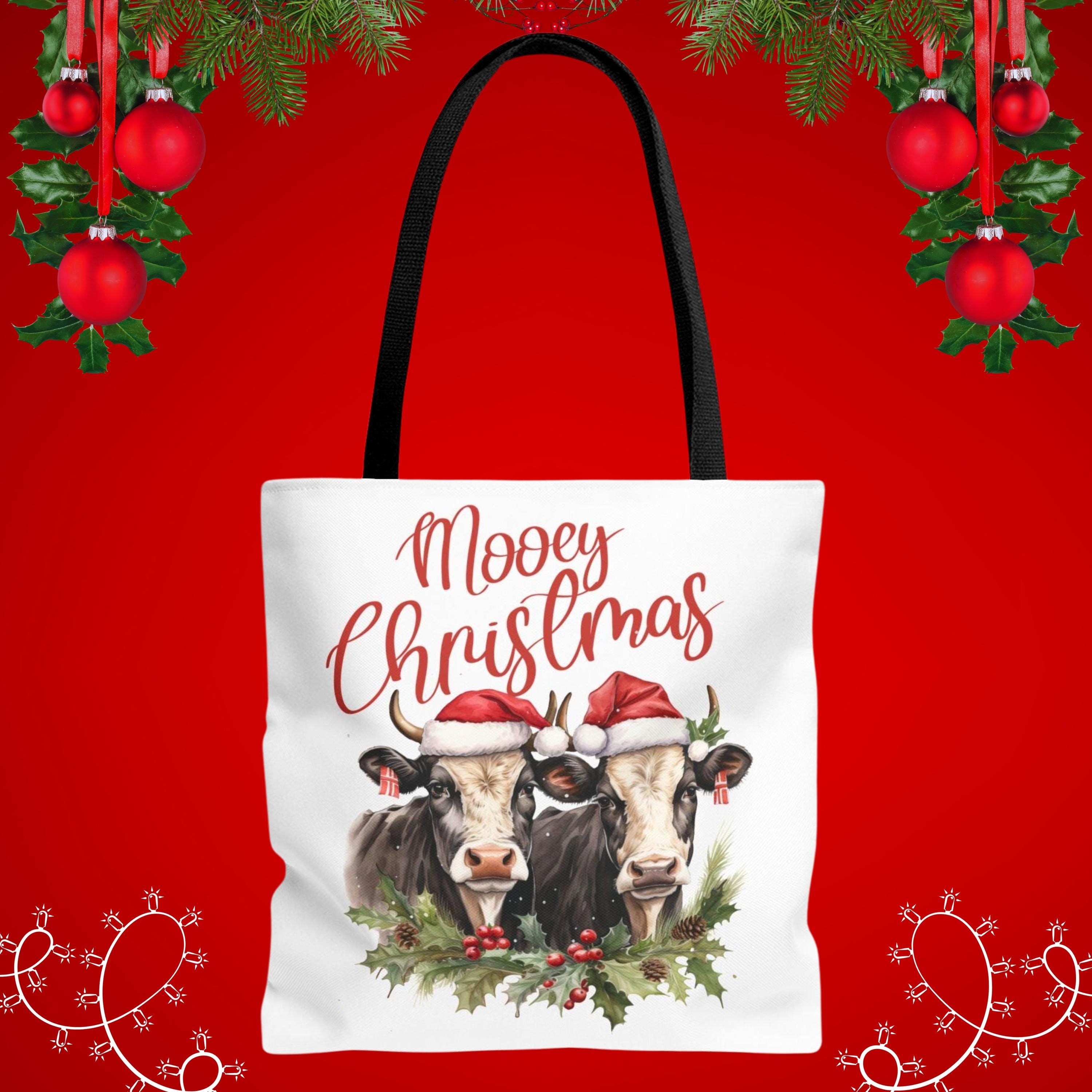A white tote bag with a Christmas-themed design featuring two cows wearing Santa hats and surrounded by holly and berries.