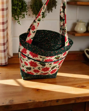 A hand-sewn tote bag with a floral pattern sits on a wooden surface, with a window and plants visible in the background.