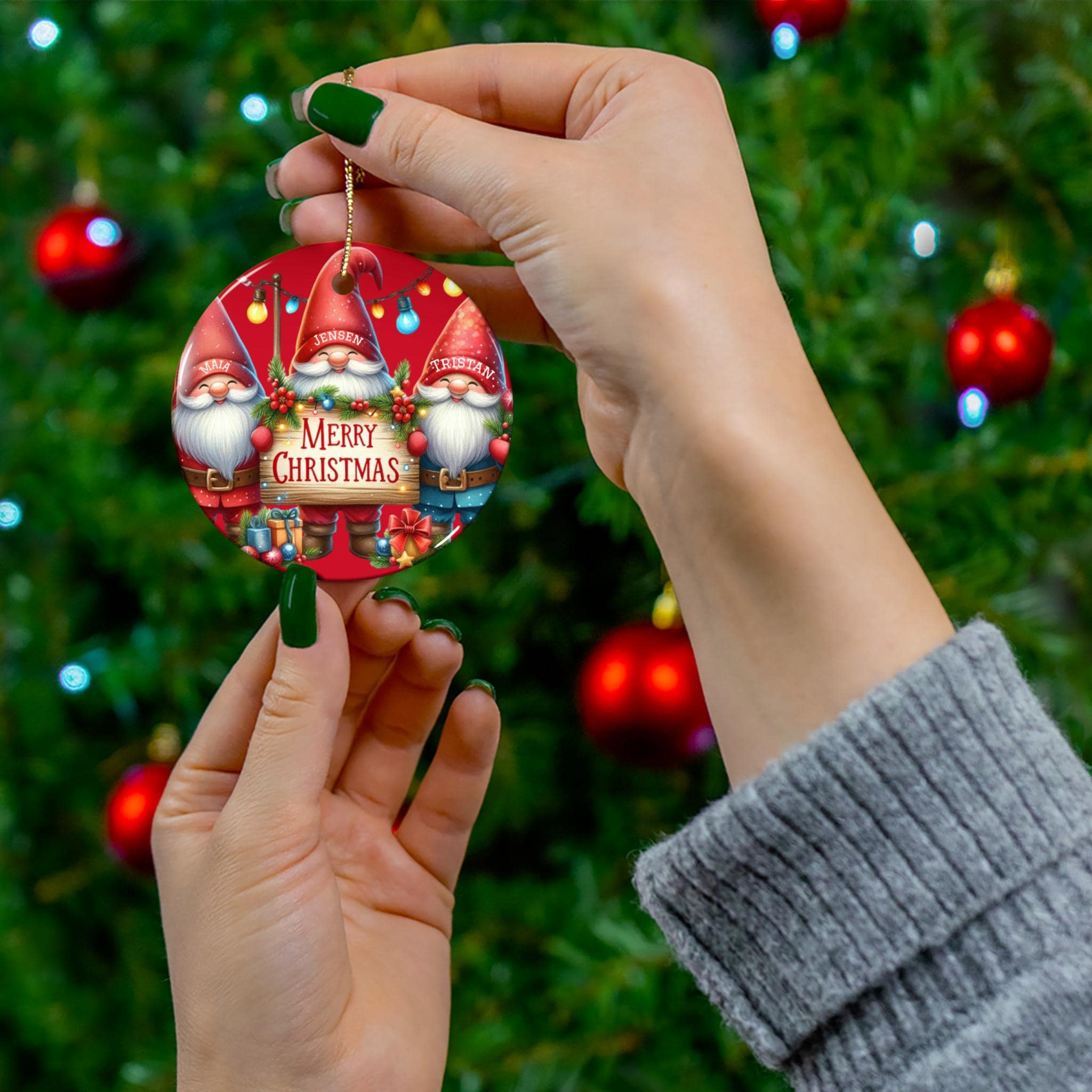 A person's hand holding a red ornament with a Christmas tree in the background.