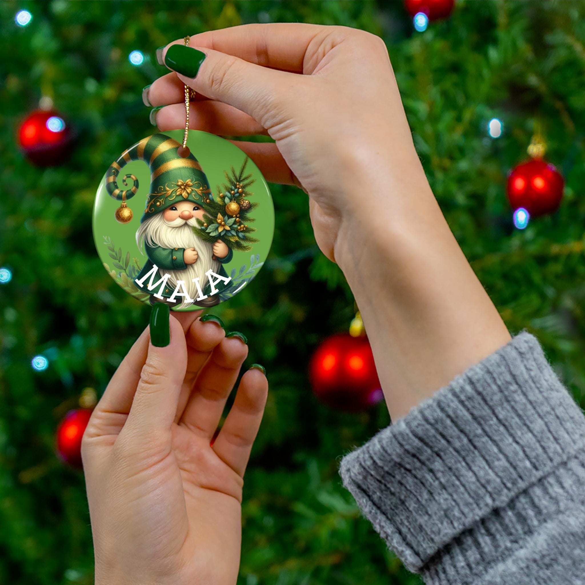 A person's hand holding a green ornament with a gnome design, with a blurred Christmas tree in the background.