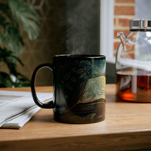 A black mug with a floral design sits on a wooden surface, with a glass kettle and a stack of papers nearby.