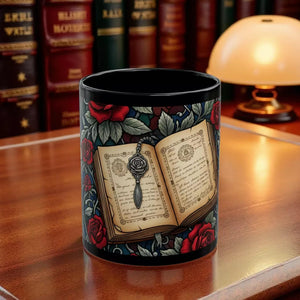 A black mug with a floral design featuring an open book with a rose and a key, surrounded by red roses and leaves.