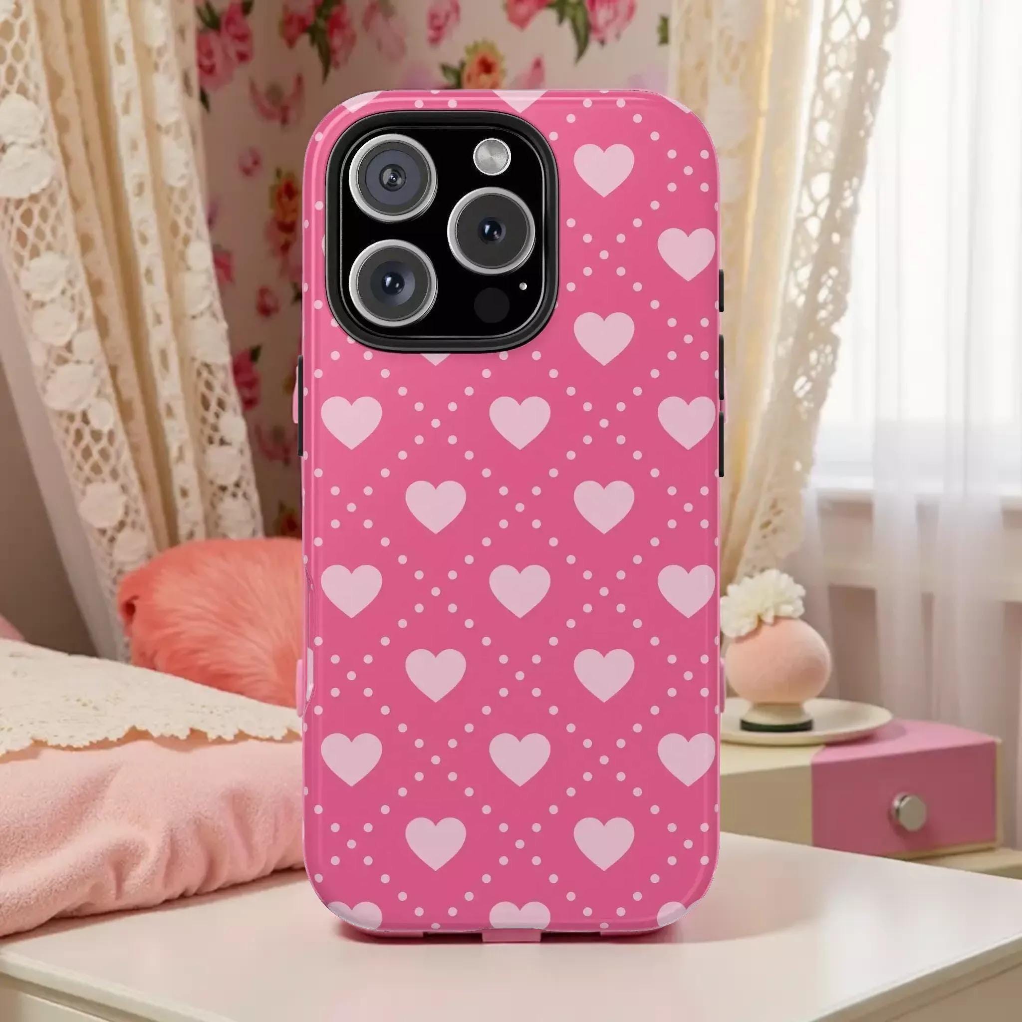 A pink phone case with a polka dot pattern and hearts printed on it, placed on a white surface.