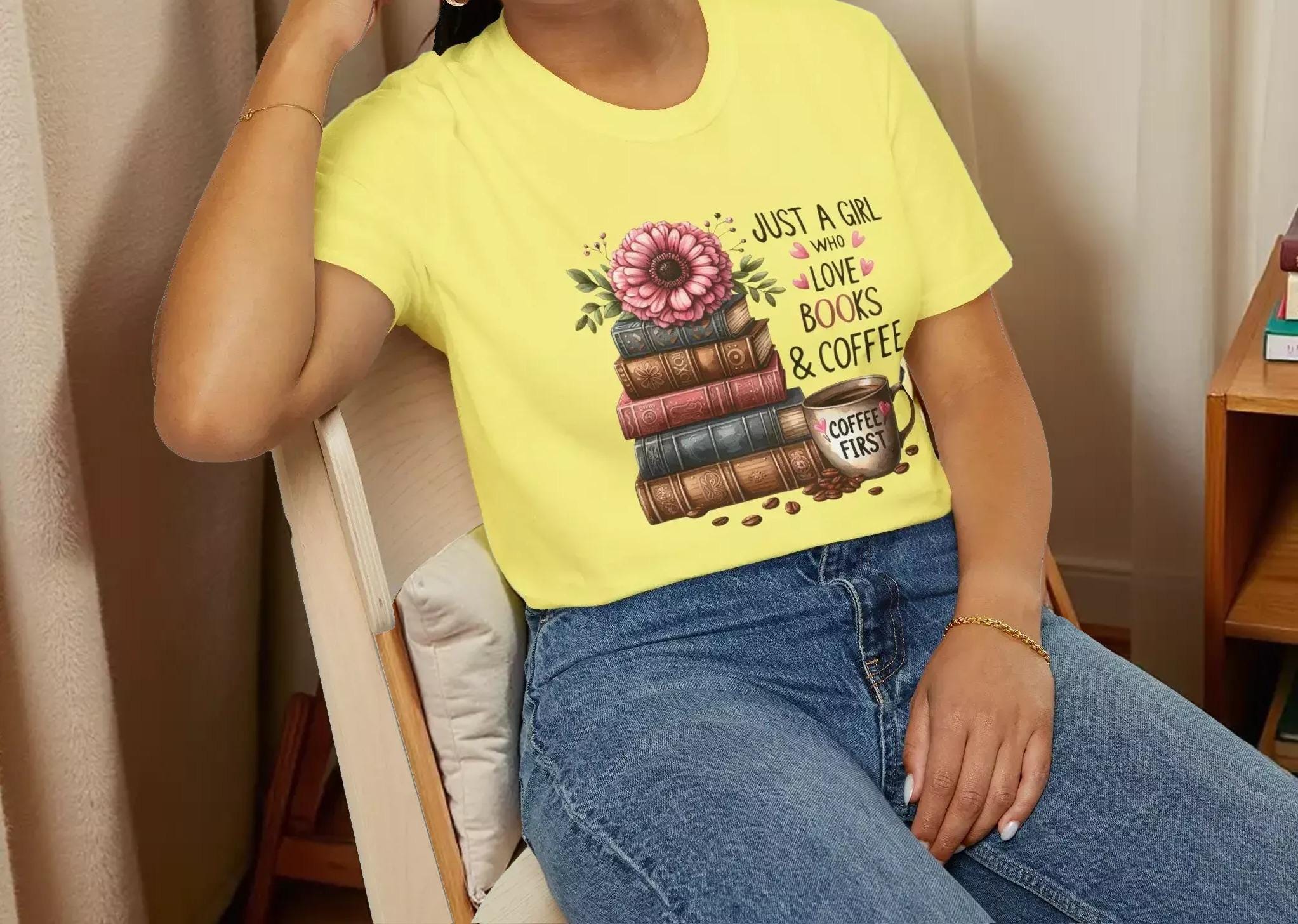 A smiling woman wearing a yellow t-shirt with a graphic design of stacked books and a flower.