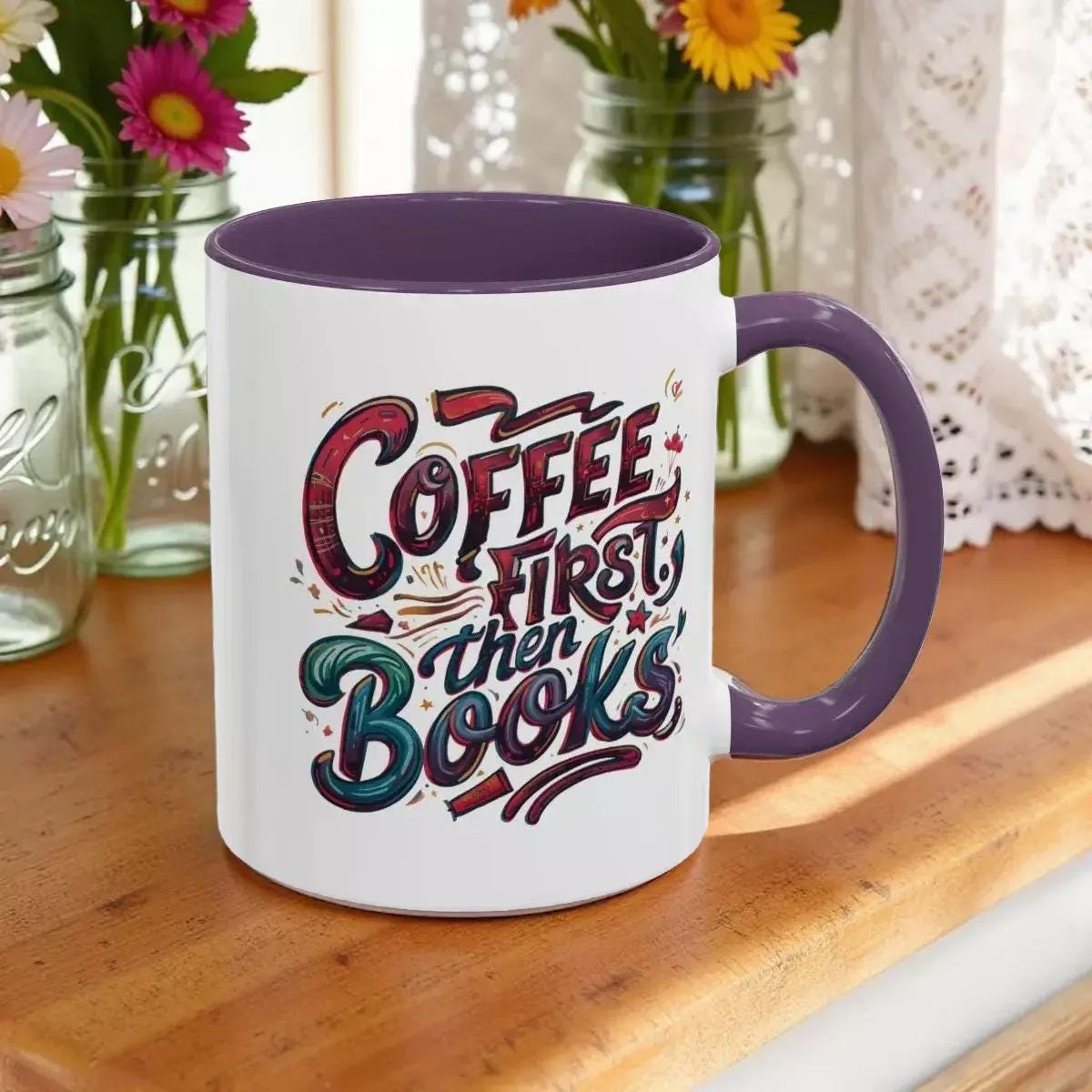 A white mug with a purple interior, featuring a colorful and stylized text design that reads "Coffee first then books".