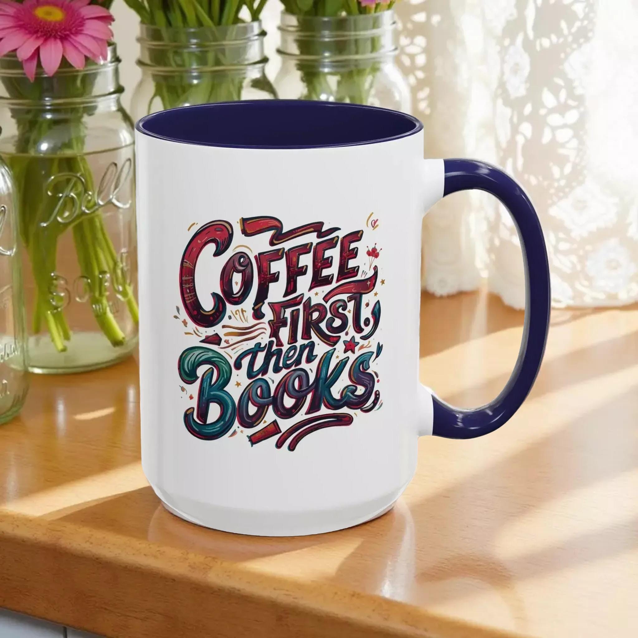A white mug with a blue rim, featuring a colorful and artistic design with the text "Coffee first then books" printed on it.