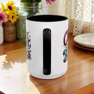 A white ceramic mug with a black handle, featuring colorful text and designs on its sides.