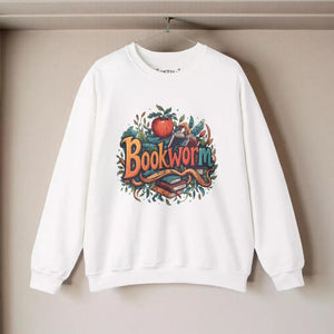 A white sweatshirt with a colorful graphic design featuring the word "Bookworm" surrounded by various objects such as books, leaves, and an apple.