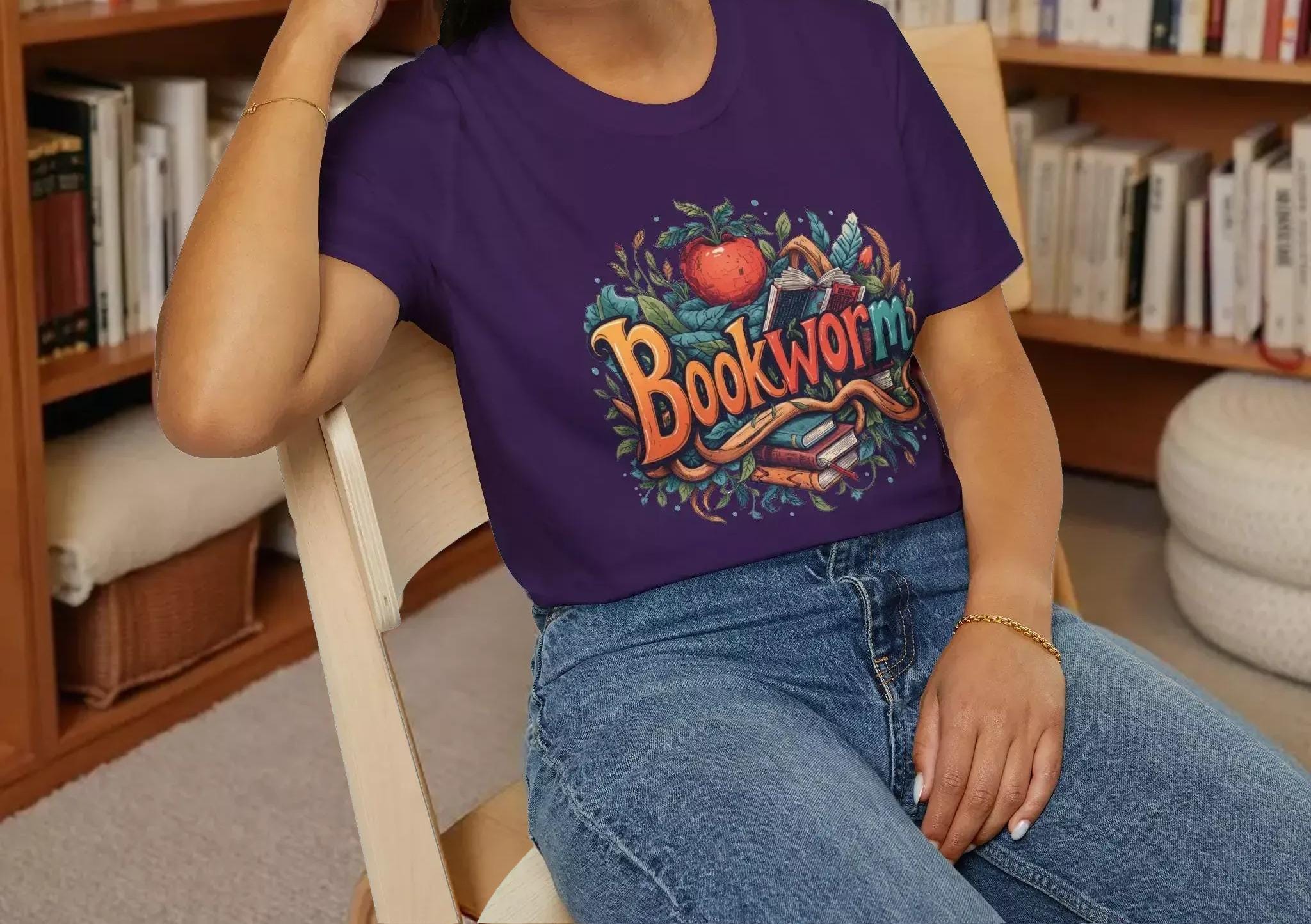 A smiling woman wearing a purple t-shirt with a colorful graphic design and sitting on a wooden chair.