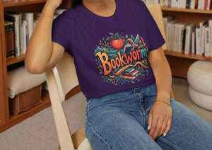 A smiling woman wearing a purple t-shirt with a colorful graphic design and sitting on a wooden chair.