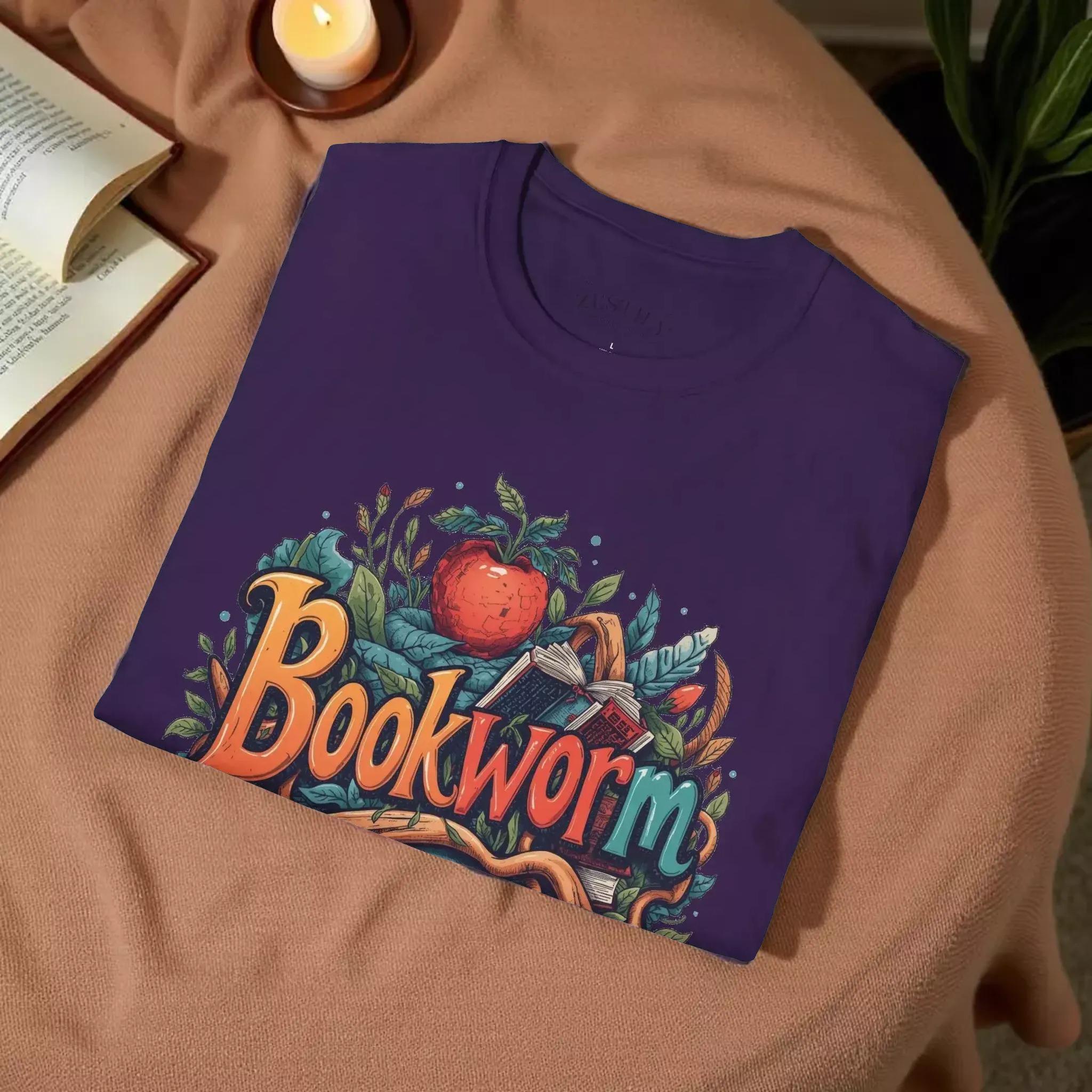 The image is a purple t-shirt with a colorful graphic design featuring the word "Bookworm" surrounded by various elements such as leaves, an apple, and a book.