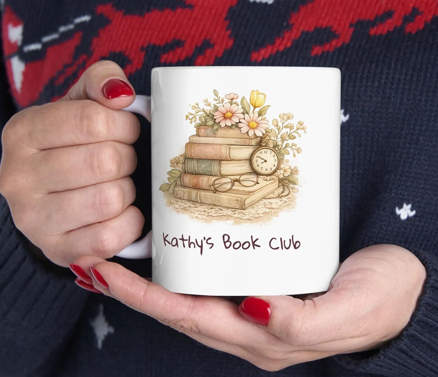 A person is holding a mug with a design of stacked books and flowers, along with the text "Kathy's Book Club".
