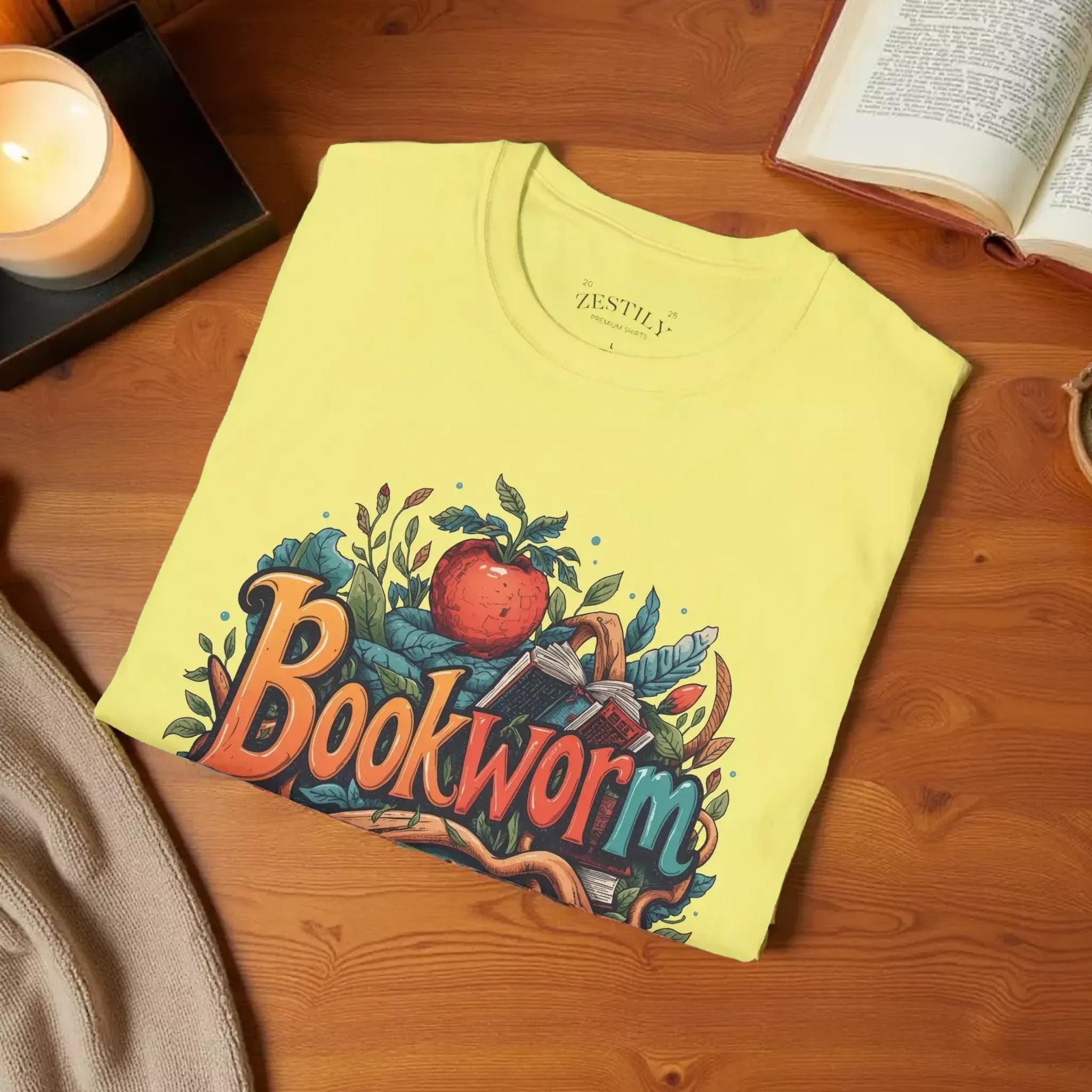 A yellow t-shirt with a colorful graphic design featuring the text "Book Worm" surrounded by various elements such as leaves, an apple, and a book.
