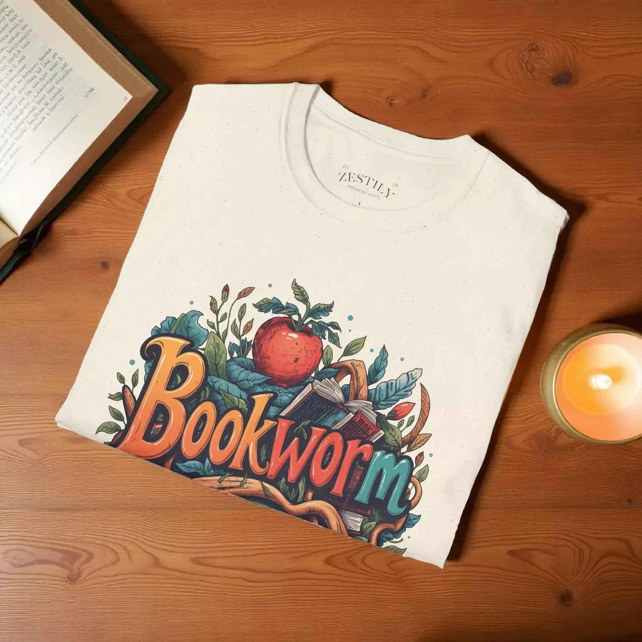 The image is a white t-shirt with a colorful graphic design featuring the word "Bookworm" surrounded by various elements such as leaves, an apple, and a book.