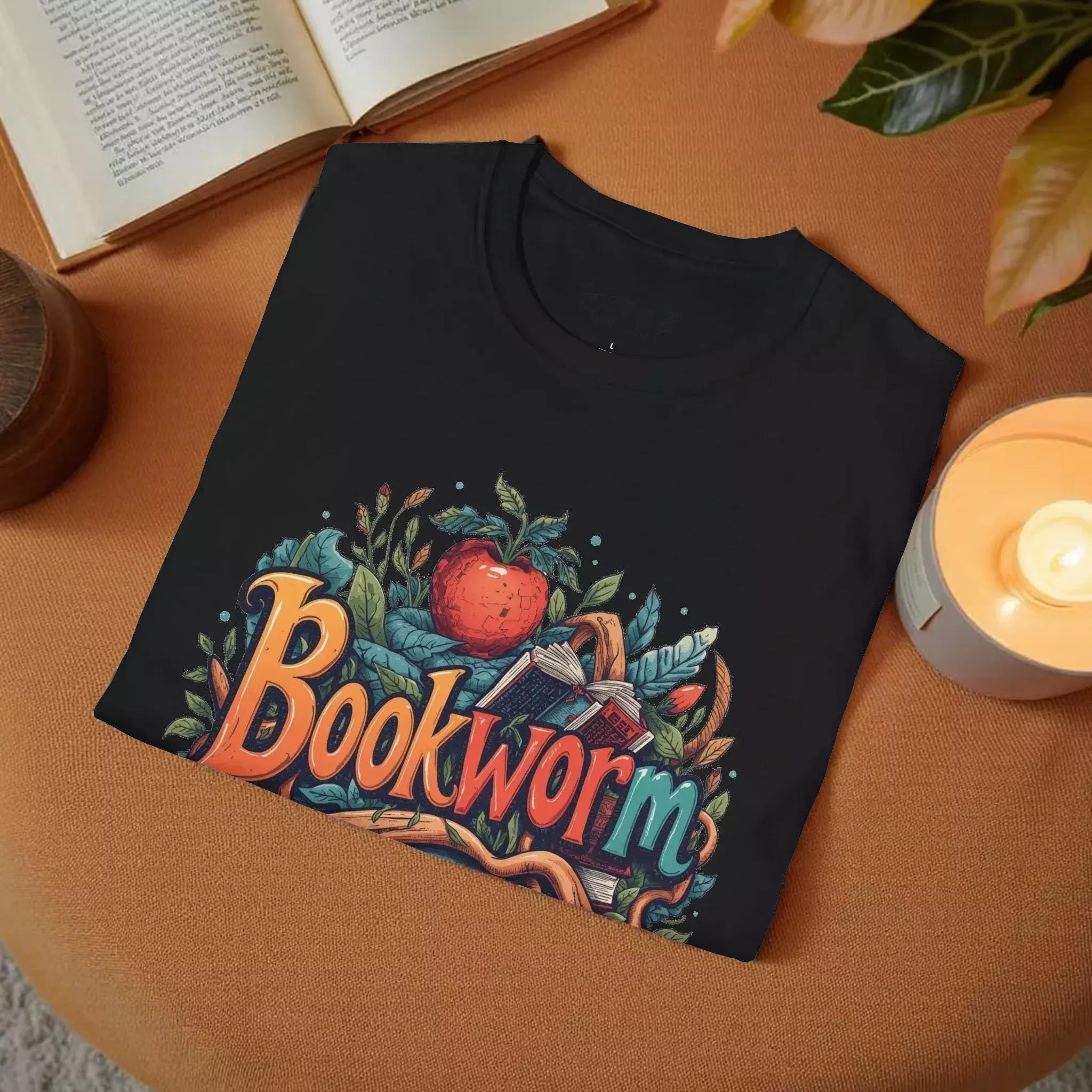 The image is a black t-shirt with a colorful graphic design featuring the word "Bookworm" surrounded by various elements such as leaves, an apple, and a book.