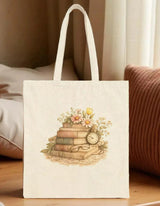 A beige tote bag with a printed design depicting a stack of books surrounded by flowers and a clock.