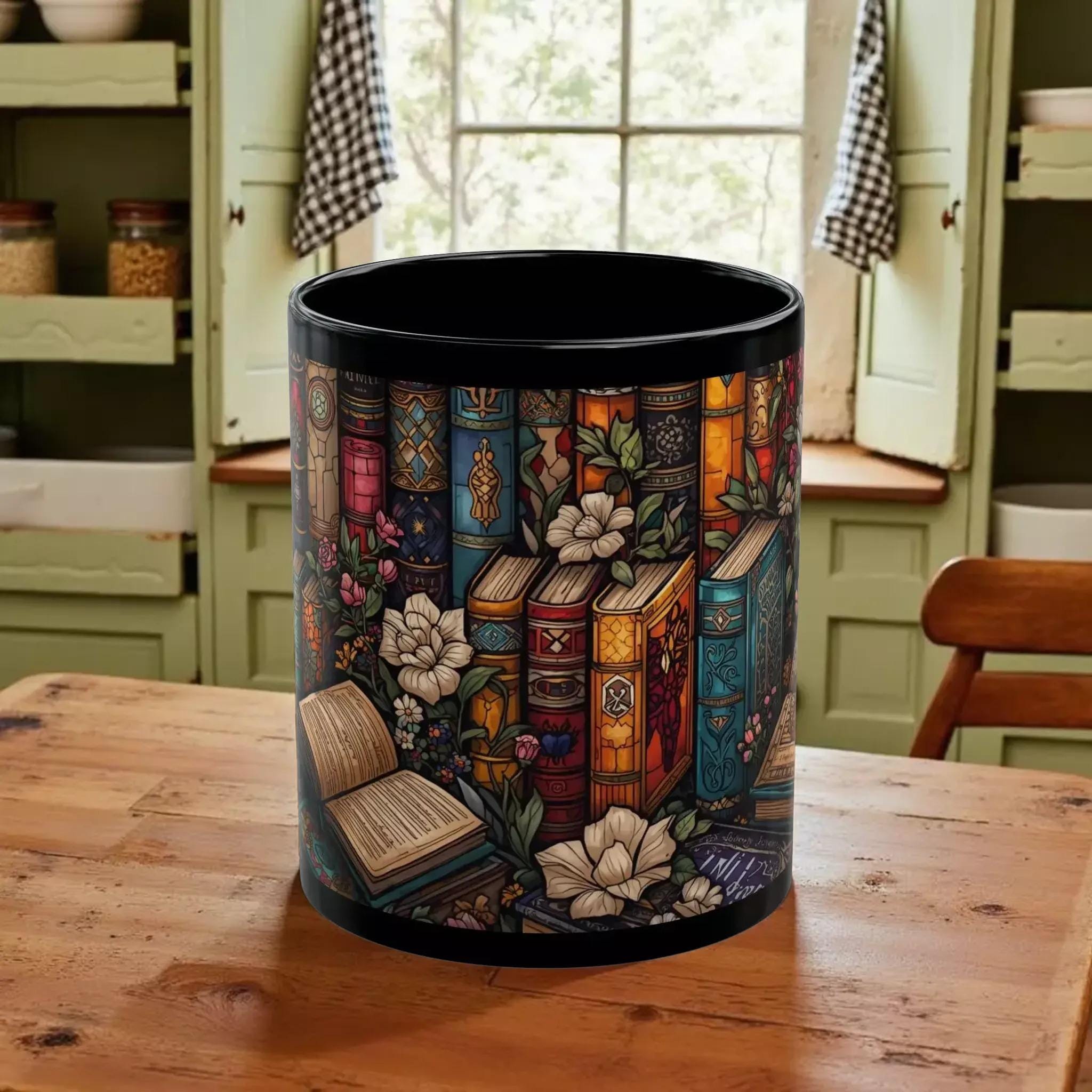 A black mug with a colorful, intricate design featuring various books, flowers, and other decorative elements.