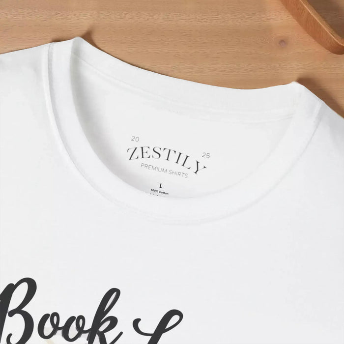 A beige t-shirt with a printed design that includes a cup of coffee, a stack of books, and flowers. The text on the t-shirt says "Book Lover".