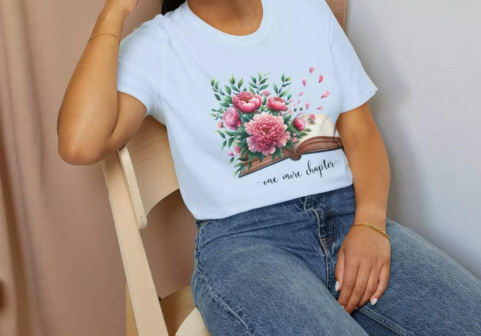 A smiling woman wearing a t-shirt with a floral design and the text "one more chapter" is sitting on a wooden chair.
