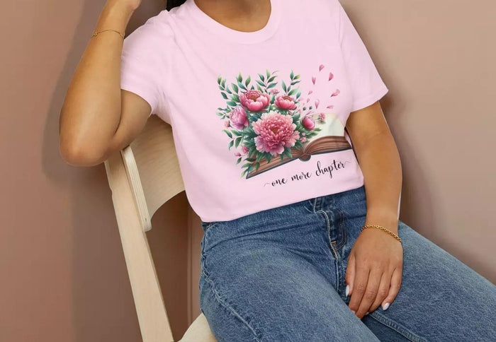 A smiling woman wearing a t-shirt with a floral design and the text "one more chapter" is sitting on a wooden chair.
