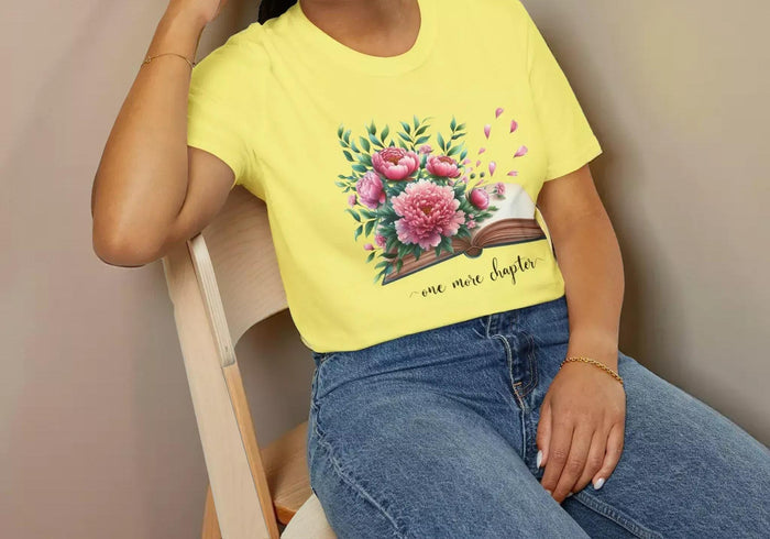 A smiling woman wearing a t-shirt with a floral design and the text "one more chapter" is sitting on a wooden chair.