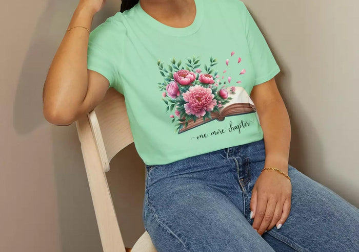 A smiling woman wearing a t-shirt with a floral design and the text "one more chapter" is sitting on a wooden chair.