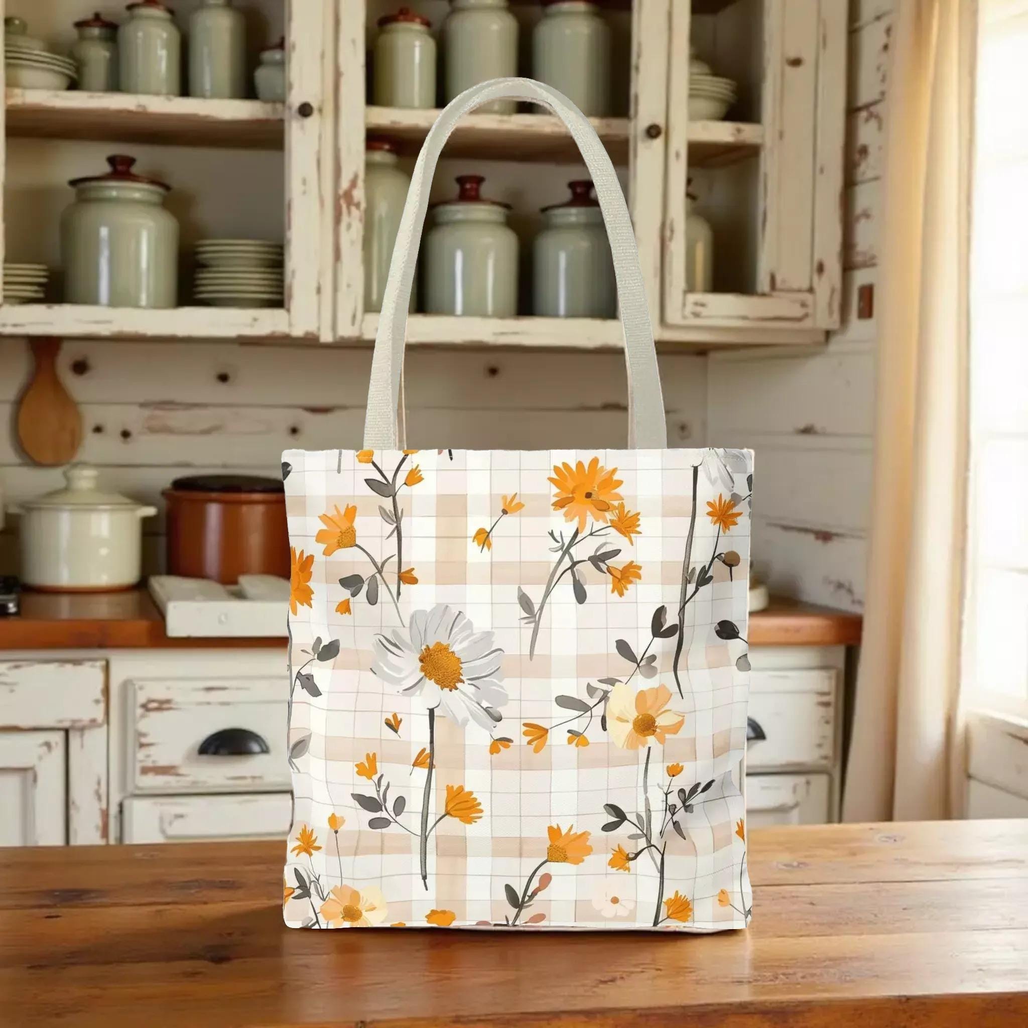 A white tote bag with a floral pattern of orange and white flowers is displayed on a wooden surface in a kitchen setting.
