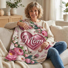 A smiling woman sits on a couch, holding a blanket with a heart and floral design.