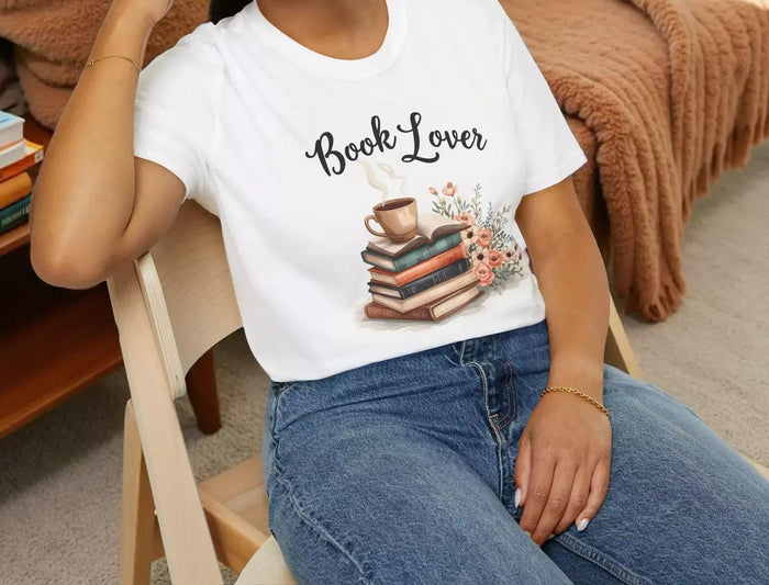 A beige t-shirt with a printed design that includes a cup of coffee, a stack of books, and flowers. The text on the t-shirt says "Book Lover".