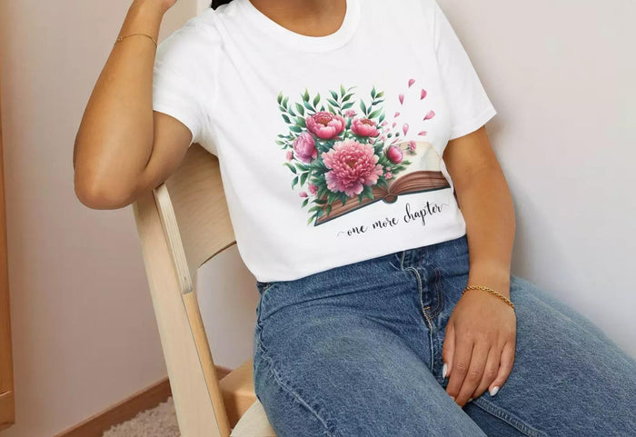 A smiling woman wearing a t-shirt with a floral design and the text "one more chapter" is sitting on a wooden chair.
