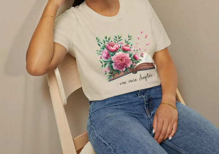 A smiling woman wearing a t-shirt with a floral design and the text "one more chapter" is sitting on a wooden chair.