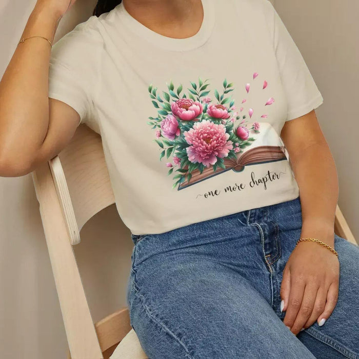 A smiling woman wearing a t-shirt with a floral design and the text "one more chapter" is sitting on a wooden chair.