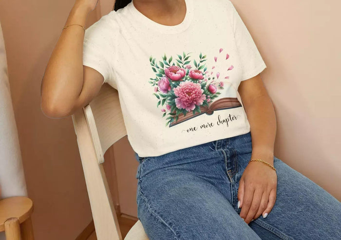 A smiling woman wearing a t-shirt with a floral design and the text "one more chapter" is sitting on a wooden chair.
