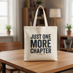 A beige tote bag with the text "JUST ONE MORE CHAPTER" printed on it in a bold, black font.