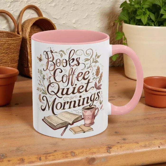 A white mug with a black handle, featuring a printed design that says "Books Coffee Quiet Mornings" along with illustrations of an open book, a cup of coffee, and a warm beverage.