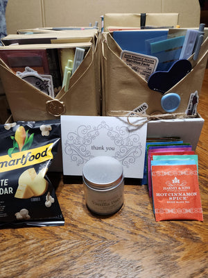 A wooden surface with various items, including a brown envelope, a small jar, a bag of popcorn, and a card with a message.