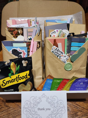 a cardboard box filled with various items, including envelopes, cards, and snacks, along with a handwritten note.