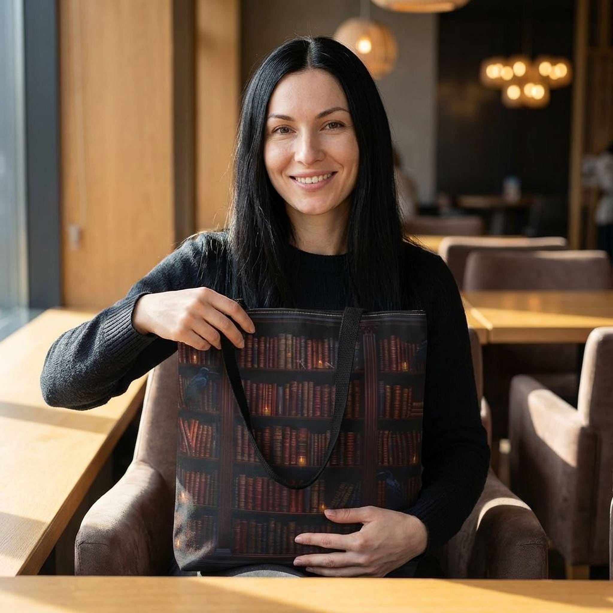 A woman with long dark hair is sitting in a chair, smiling and holding a tote bag with a book design printed on it.
