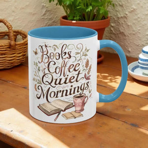 A white mug with a blue handle, featuring a design with the text "Books Coffee Quiet Mornings" and illustrations of a book, a cup of coffee, and a plant.